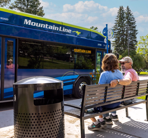 Man and woman sit on bench at bus stop as bus pulls up.