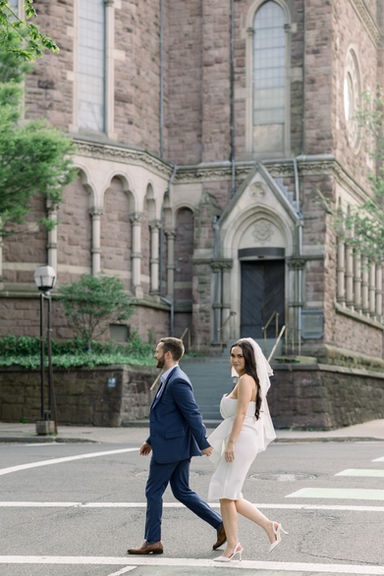 Les mariés traversent la rue, main dans la main, près d'une église.