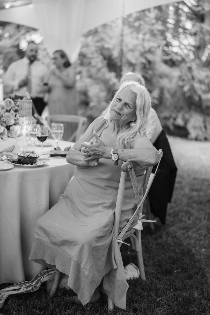 Une femme assise à une table de mariage écoute les toasts. Mariages, pose pensive dans un jardin.