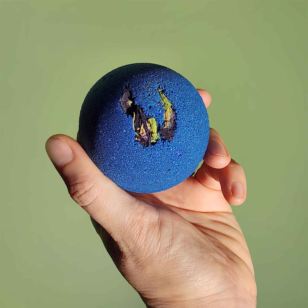 deep blue bath bomb with dried pea flowers on top held in a hand on a plain green background