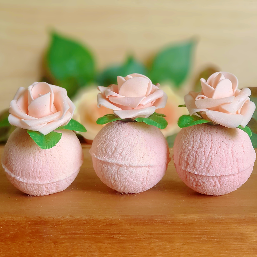 Thumbnail: dusty pink round bath bombs with pink foam roses on top placed in a row on a wooden surface