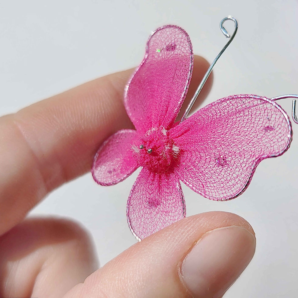 Thumbnail: pink butterfly made of mesh fabric and wire being held in a hand on a white background