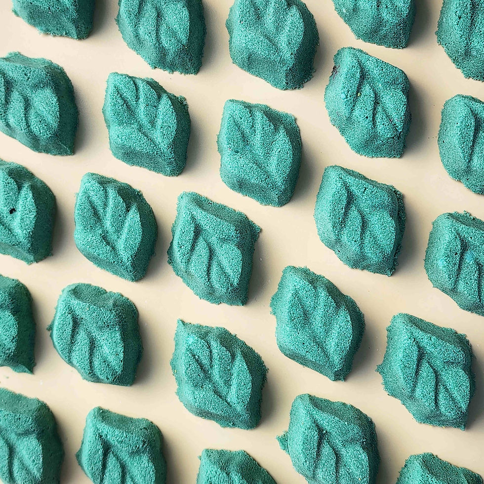 teal leaf shaped mini bath bomb laid out in a neat array over a plain beige background