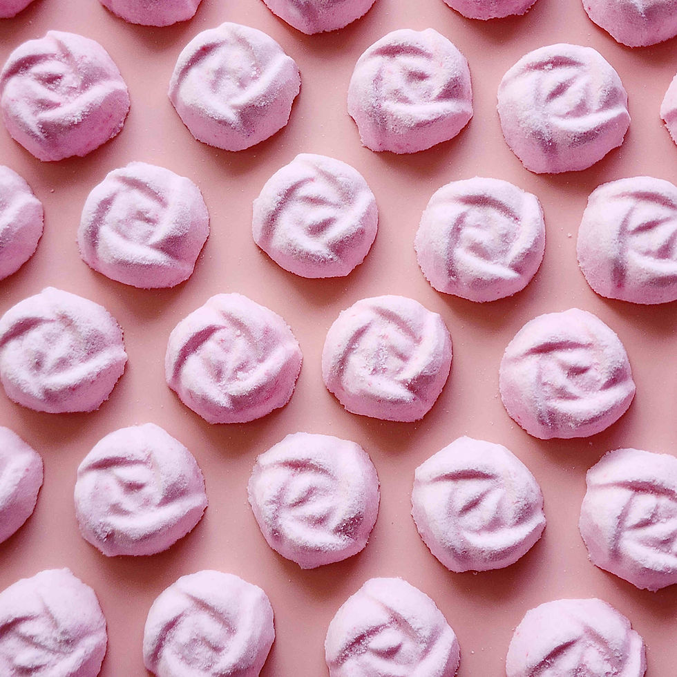 light dusty pink coloured mini bath bombs in the shape of roses laid out neatly on a plain pink background