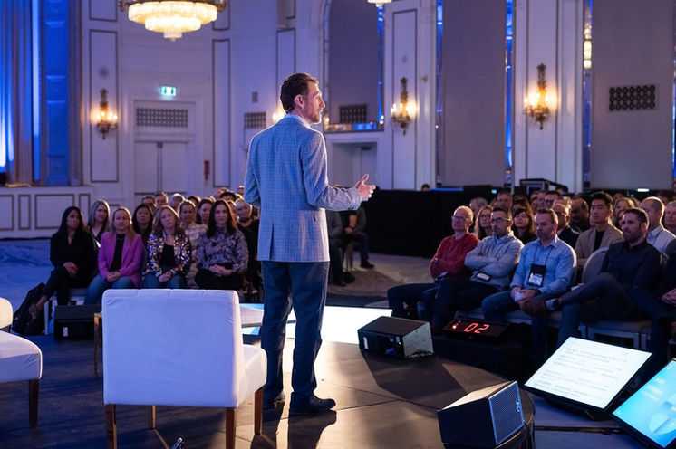 wide shot from behind of speaker on stage and attendees at a corporate event