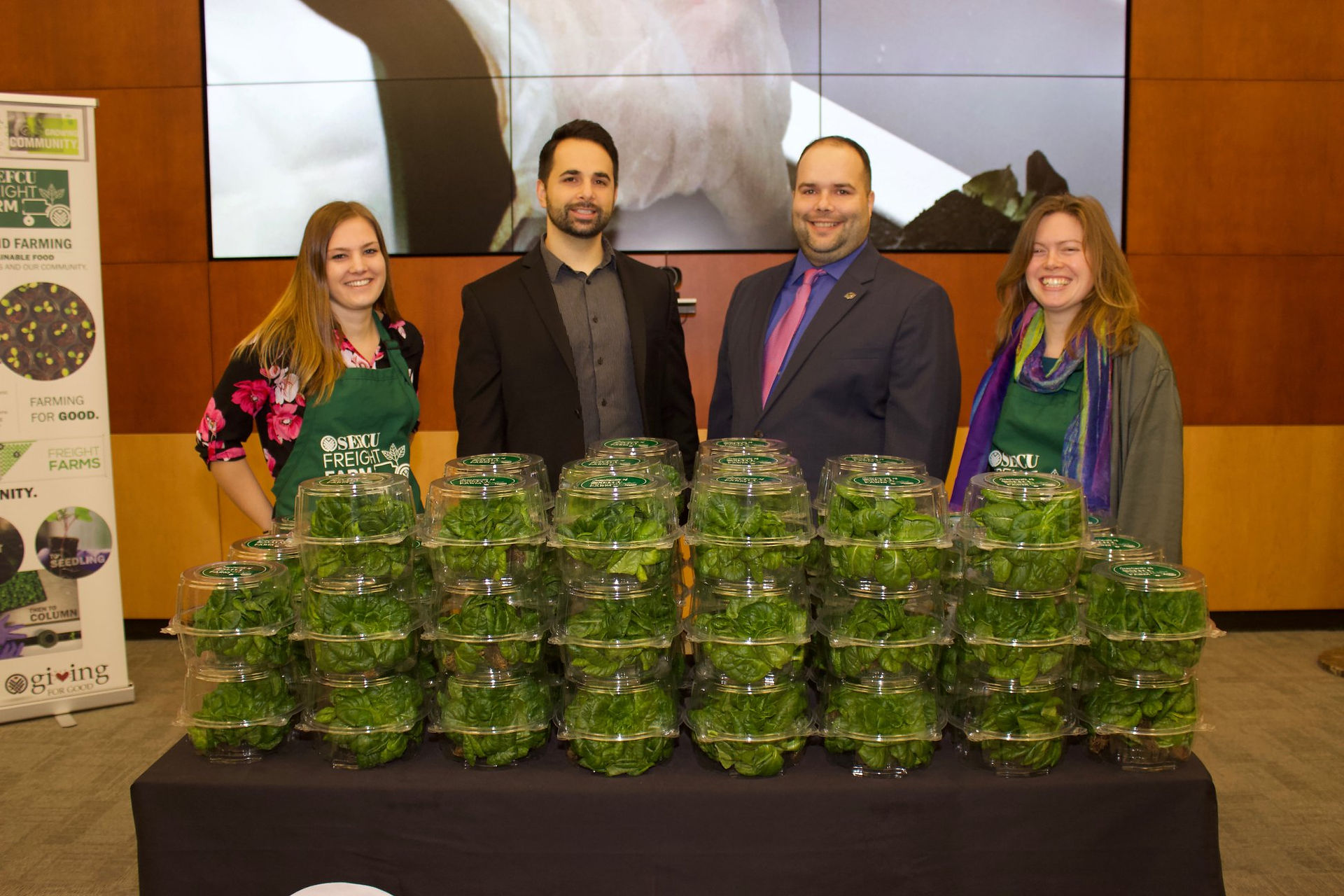 People standing in front of stacked greens, Whole Foods Market logo visible.
