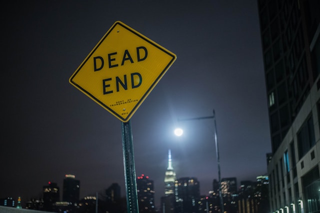 Yellow “DEAD END” road sign glowing at night against a dark city skyline, symbolising the moment someone decides to stop repeating destructive comparison cycles, self-doubt, and Grey Grid thinking patterns.
