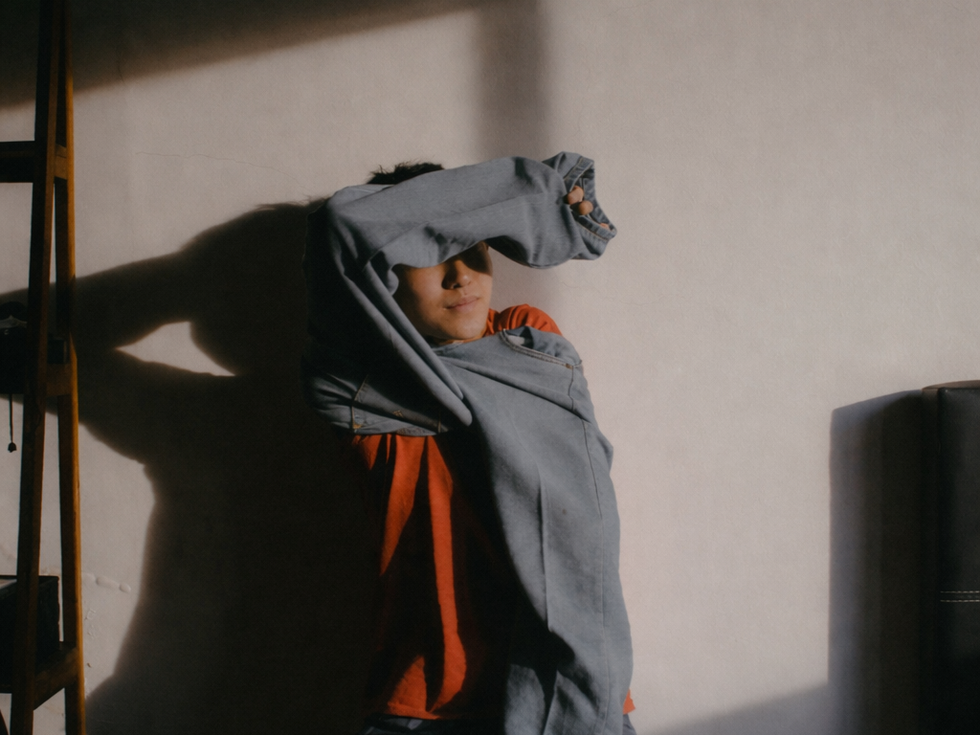 Woman standing in shadow covering her face, symbolising negative self-talk and the inner critic explored through structured journaling prompts.