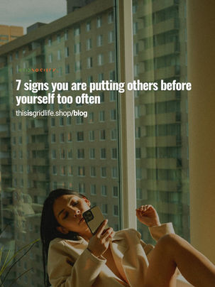 Woman sitting by a window looking at her phone, reflecting on putting others before yourself and feeling emotionally distant.