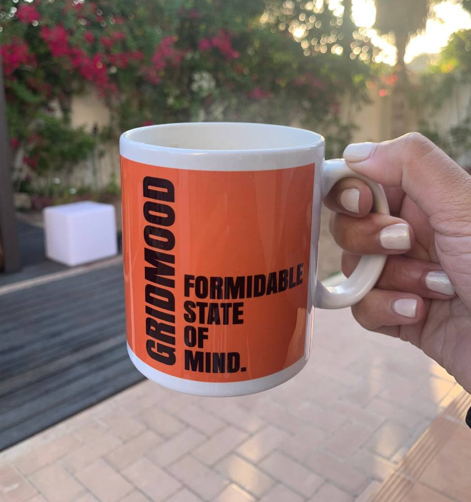 Hand holding an orange “Formidable State of Mind” mug outdoors in the morning sunlight.