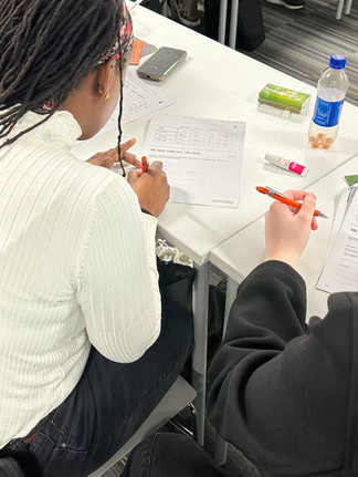 “Two attendees working through their Grid Society worksheets during a live workshop, writing reflections and organising their thoughts as part of the inner work process.”