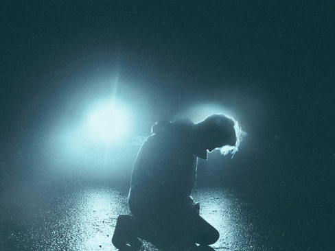 Silhouette of person kneeling, overwhelmed in emotional spiral, spotlighted by car headlights