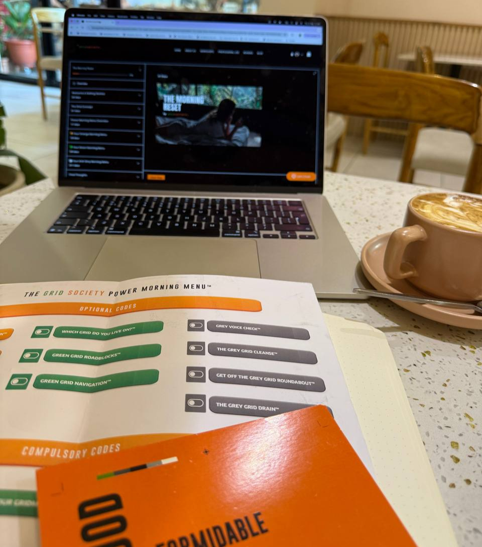 Laptop displaying the Grid Society site beside the Morning Reset workbook showing grey and green thinking sections.