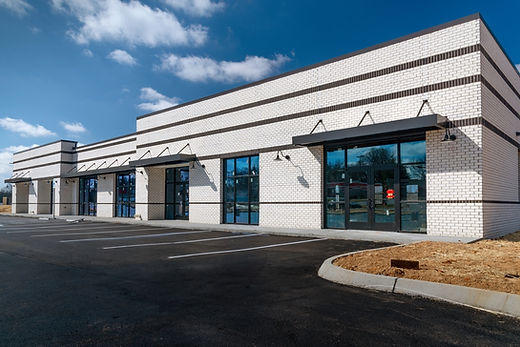 Modern white brick commercial building with glass windows and black awnings against blue sky