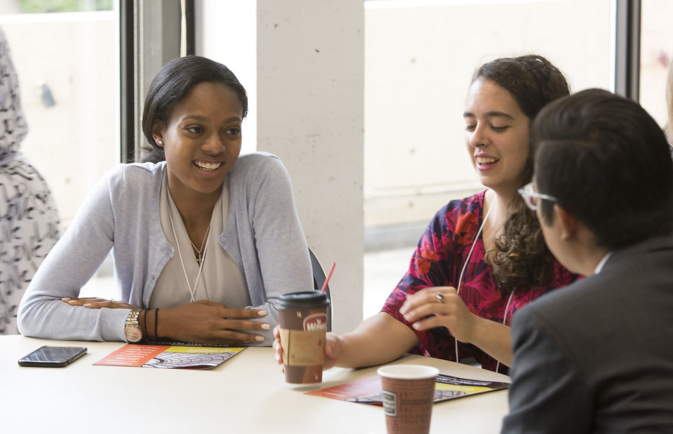 Three people are smiling and talking at a table with coffee cups present.