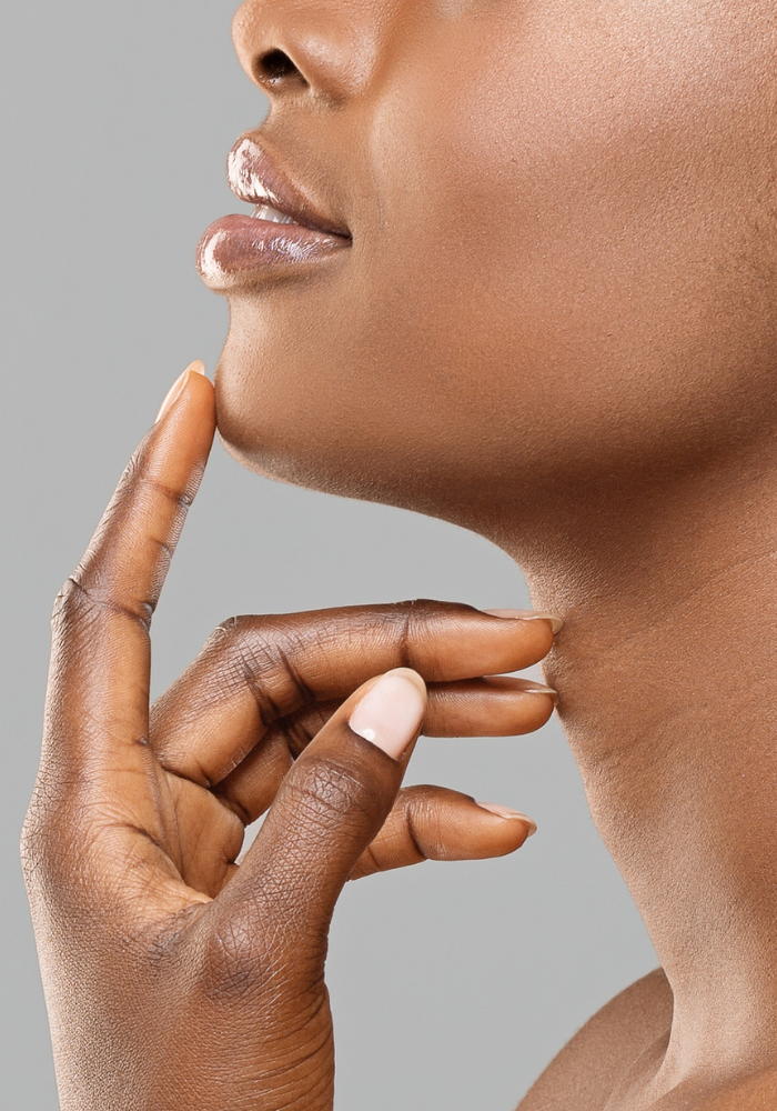 A woman with beautiful skin rests the fingers of her left hand on her chin and neck.