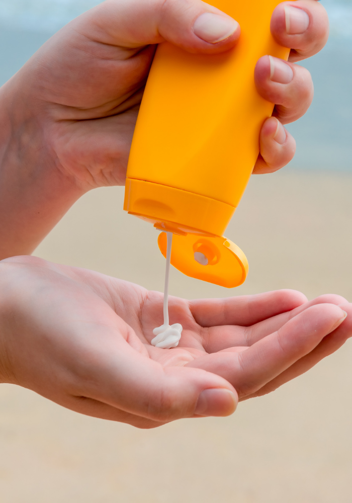 An orange bottle of sunscreen being squeezed into a hand at the beach.