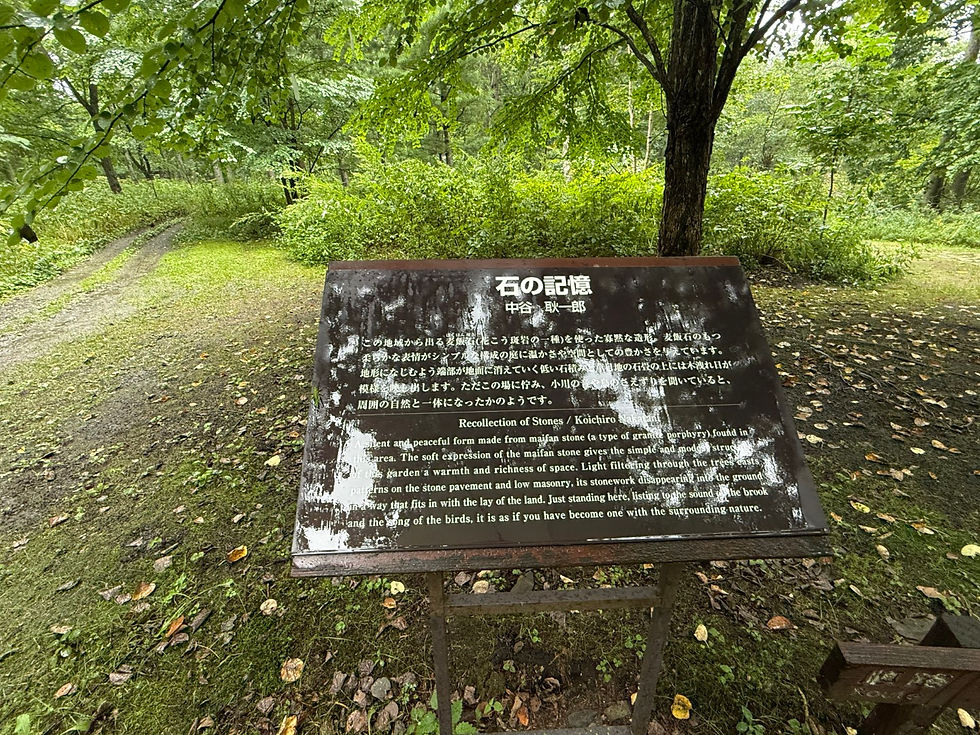 緑深い森の小道脇に案内板 石の記憶 が立ち、英題 Recollection of Stones も見える。落ち葉の地面に静かな雰囲気。