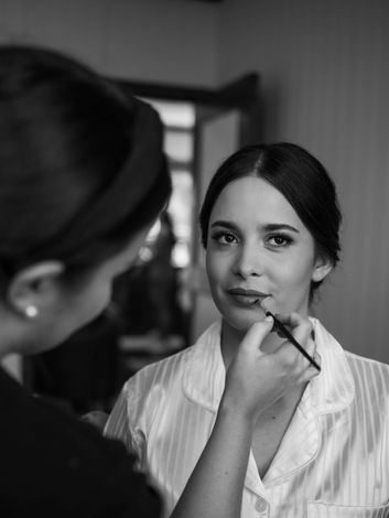 Professional makeup artist applies lipstick to woman in black and white.