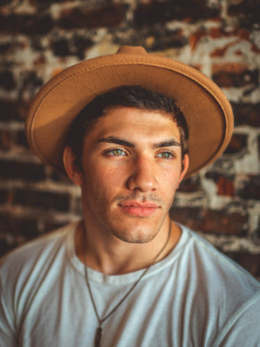 Headshot of man in hat in front of brick wall