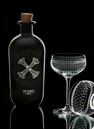 Bumbu XO Rum bottle with crystal glasses on reflective black surface using white edge lighting