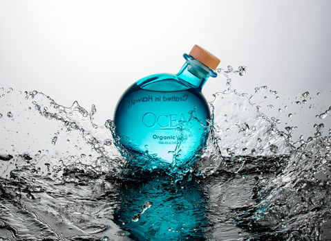 Ocean Organic Vodka bottle mid-splash on black plexiglass with white background