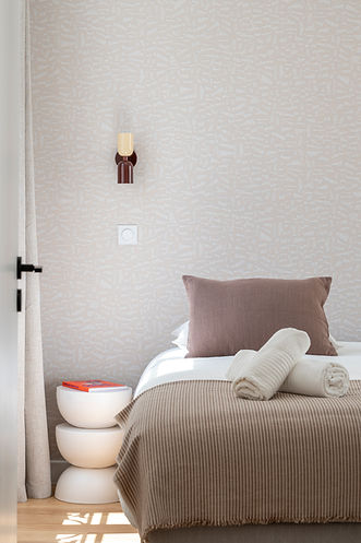 Chambre lumineuse avec lit beige, table d'appoint design et lampe murale moderne, dans un appartement 2 pièces de 45m².