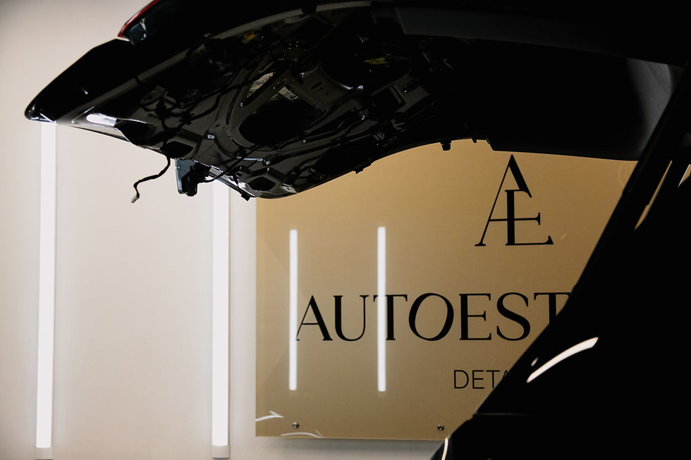 Atvērts auto motora pārsegs tumšā telpā ar zīmola zīmi Autoestetika fonā. Aptumšots apgaismojums un vertikālas gaismas joslas.