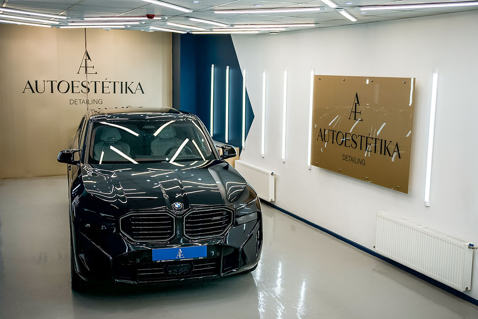 Glancīgs melns BMW stāv apgaismotā centrā ar zīmolu Autoestētika uz sienām. Gaiša telpa, mūsdienīgs dizains.