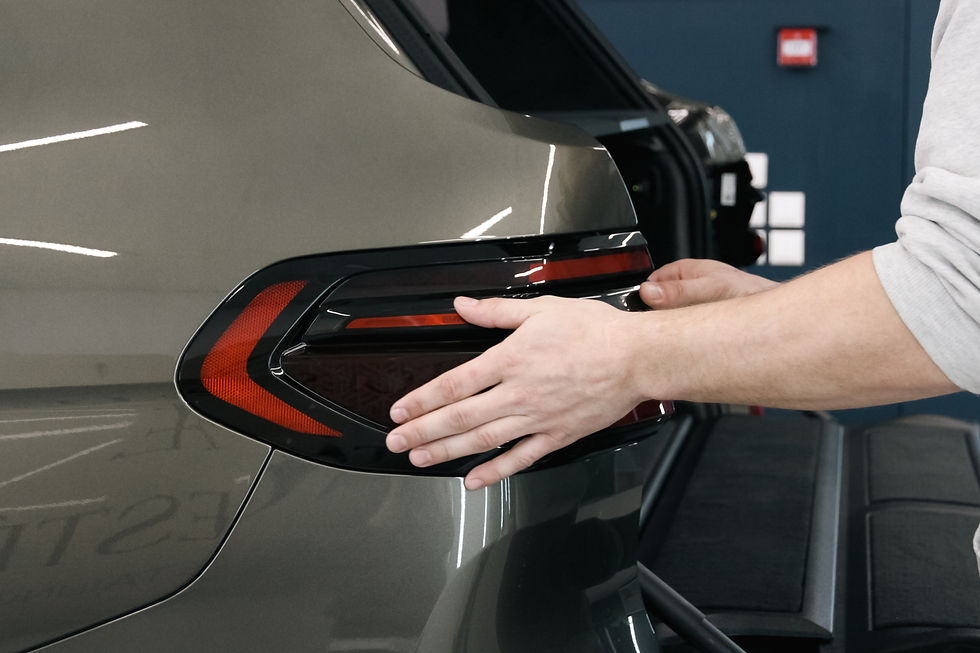 Cilvēks ar rokām piestiprina auto aizmugurējo lukturi pelēkai mašīnai autosalonā.