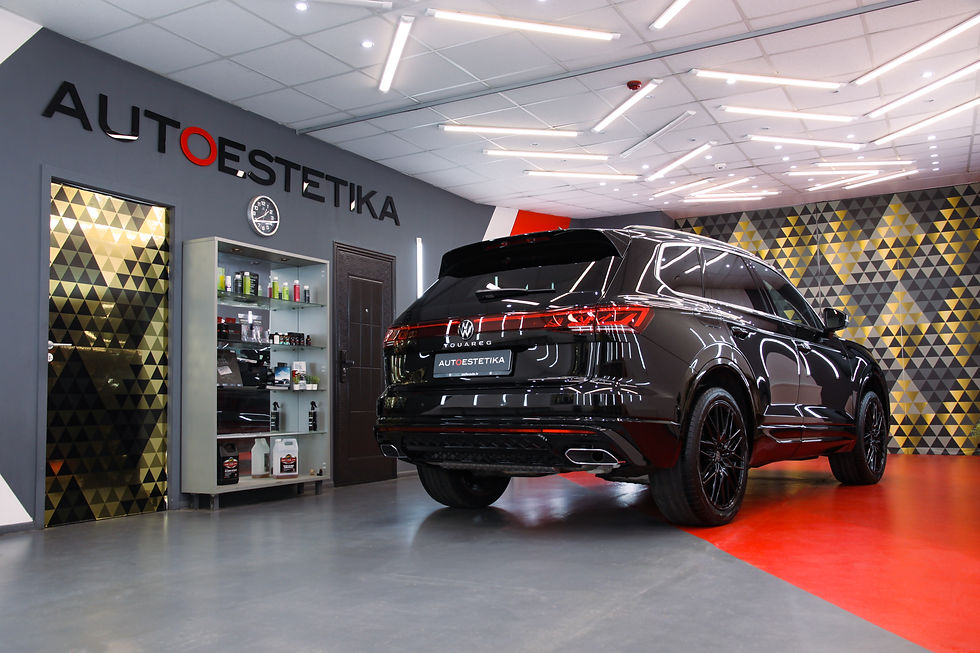 Melns SUV modernā garāžā ar uzrakstu AUTOESTETIKA. Fonā ir trīsstūrveida raksts uz sienas, plaukts ar auto kopšanas līdzekļiem.