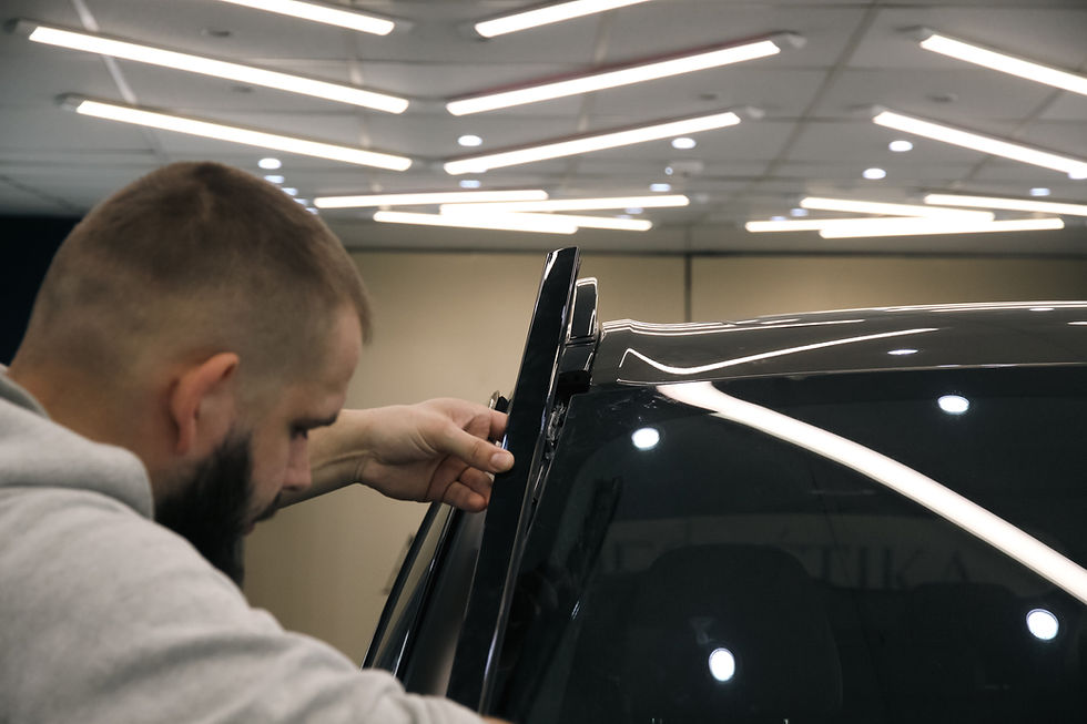 Vīrietis telpā regulē melna auto jumta detaļu zem spilgtām griestu lampām.