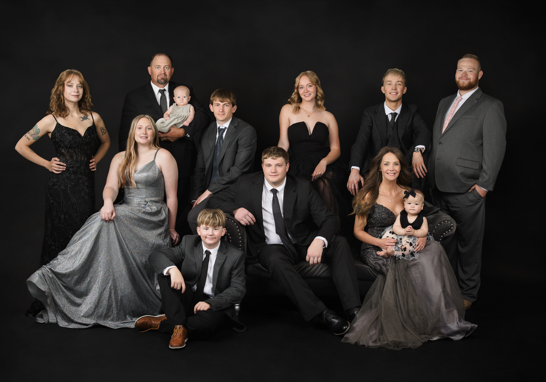 Formal family portrait with parents, older children, and a baby posed in black attire against a dark studio background at La Bella Sole Photography