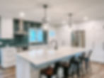 Kitchen island with overhead lights and green backsplash at the sink.
