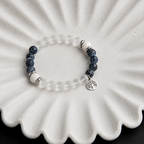 Détail d’un bracelet en lave blanche, agate craquelée bleu foncé et perle en verre transparente