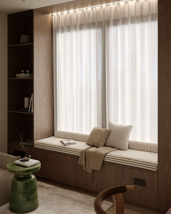 Close-up of a built-in window seat in a contemporary apartment, showing striped cushions, a green ceramic side table, and sheer white curtains.