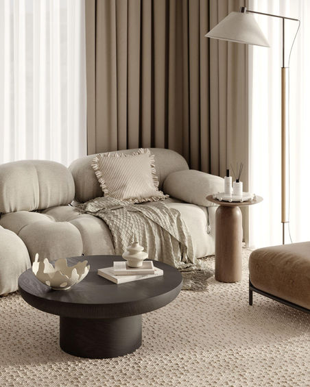 Detail of the modern living room area with a textured rug, black coffee table, side table, and part of a modular sofa.