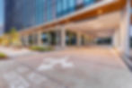 Modern glass office entrance with covered drive, EXIT and DO NOT ENTER signs, white directional arrows, empty at dusk