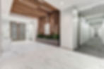Bright modern office hallway with marble floor, wood slat ceiling, planter, floor 7 sign, trash bin, and restroom corridor.
