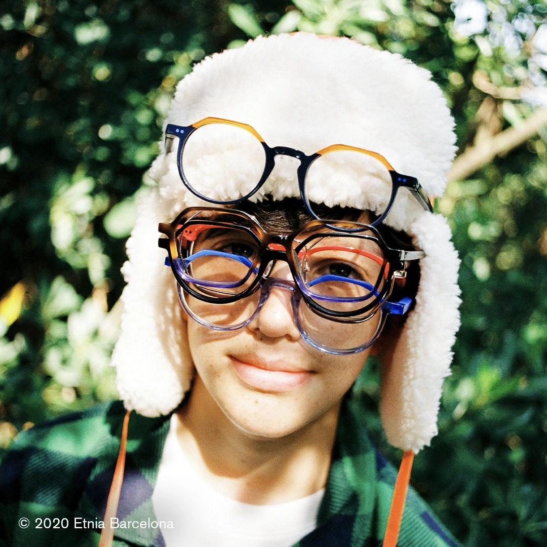 smiling boy in sherpa hat wearing many pairs of eye glasses