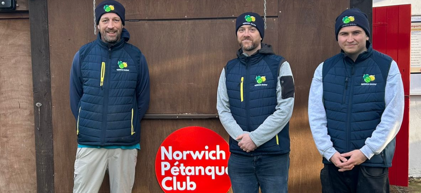 Tom Ralph, Gavin Seymour, and Jonathan Gracie in Onions uniform standing in front of the Norwich Petanque sign.