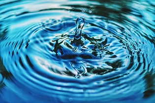 Goutte d’eau tombant dans l’eau bleue, créant des ondulations concentriques en gros plan.