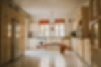 Woman levitating in kitchen, arms outstretched, near cabinets and windows indoors.