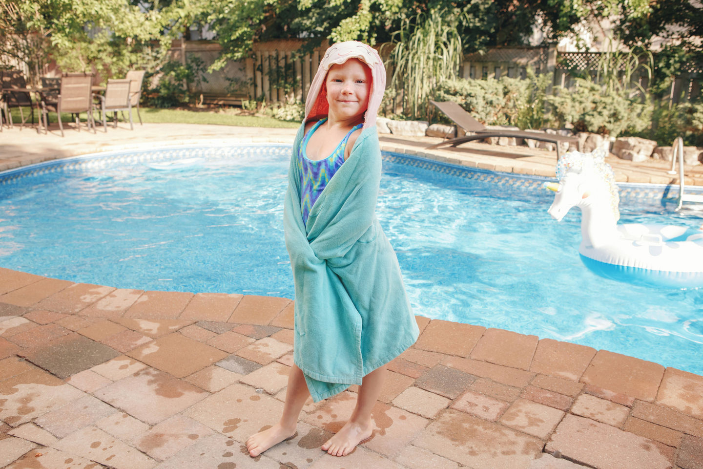 Young girl in pool towel smiling next to a swimming pool.