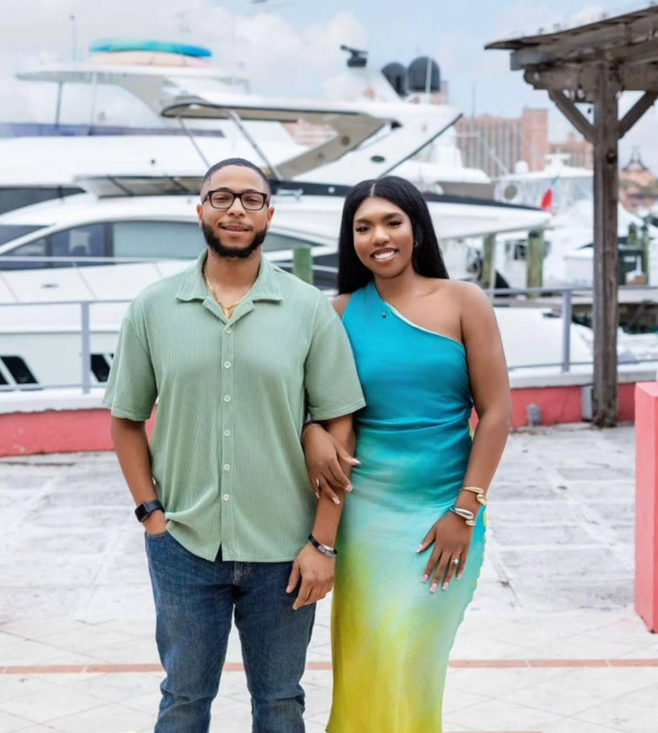 Couple standing together, smiling with a yacht background, Jewels by the Sea.