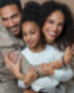 Smiling family of three embraces for a portrait, includes daughter, mother, father.