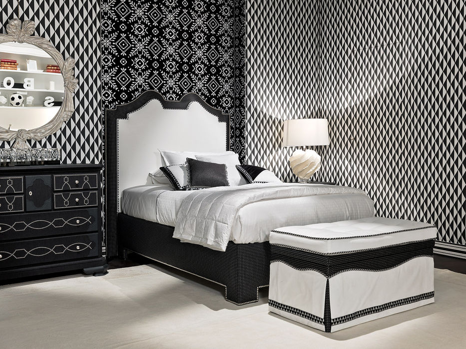 Bed with a black, decorated nightstand, a round mirror with a carved frame, and a wall featuring black-and-white geometric patterned wallpaper.