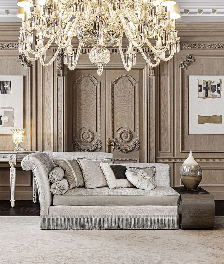 Gray chaise lounge with pillows in an elegant living room with a large chandelier, wooden paneling, and a vase on a side table.