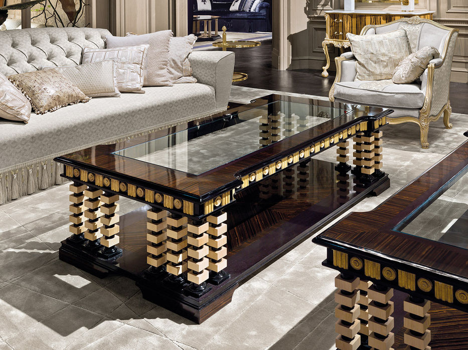 Rectangular polished ebony coffee table with a glass top and gold decorative details, set in an elegant classic living room with an ivory sofa and armchair.