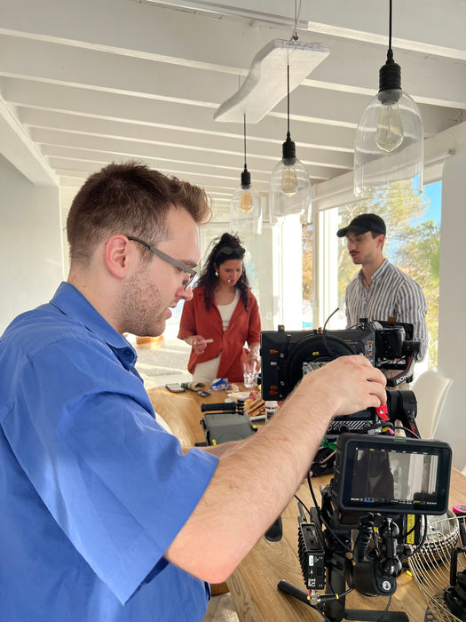 Tournage film: caméraman ajustant l'équipement, deux acteurs en arrière-plan.